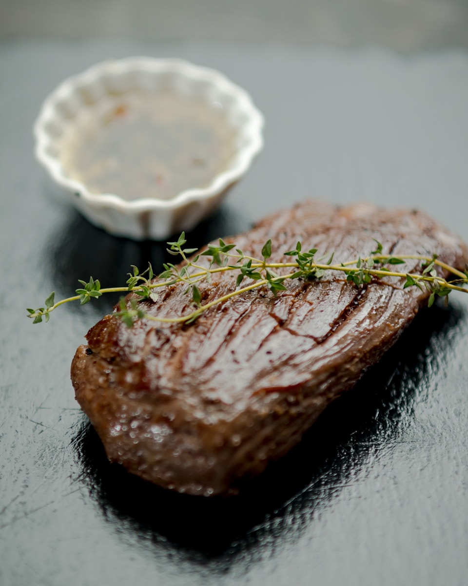 a piece of steak next to a small bowl of sauce