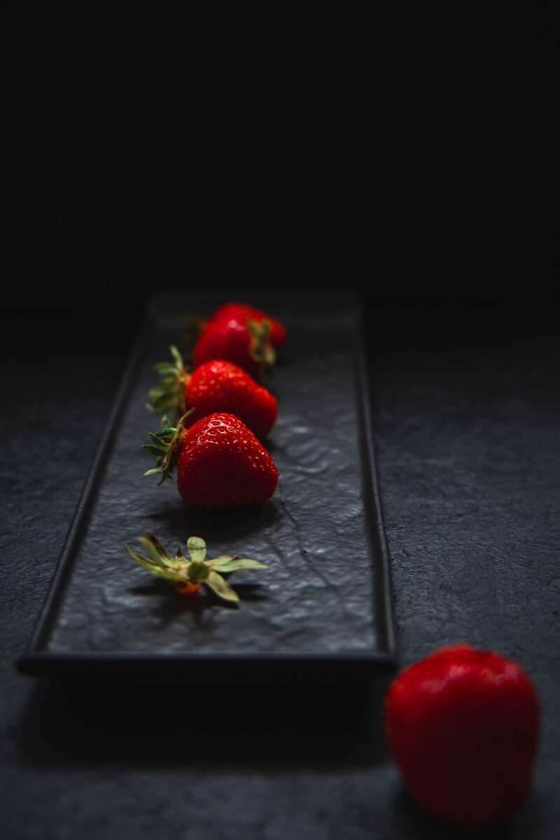 Fresh red strawberries arranged on a dark rectangular plate.